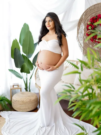 A radiant portrait in a boho-chic setting. The mom-to-be wears a white two-piece outfit that beautifully showcases her bump, surrounded by natural textures.