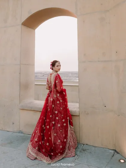 The bride looking back through an archway, her red lehenga a vibrant splash of color against the neutral tones of the architecture.
