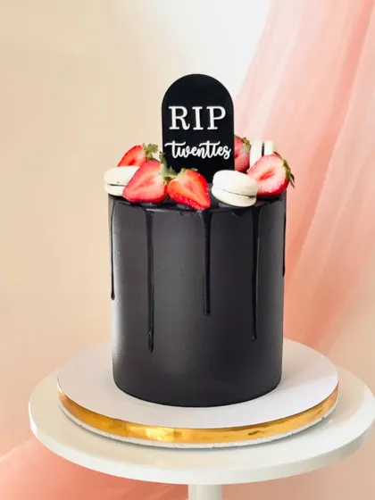 A humorous "RIP Twenties" cake for a 30th birthday. The sleek black buttercream, black chocolate drip, and fresh strawberries create a dramatic and elegant look.