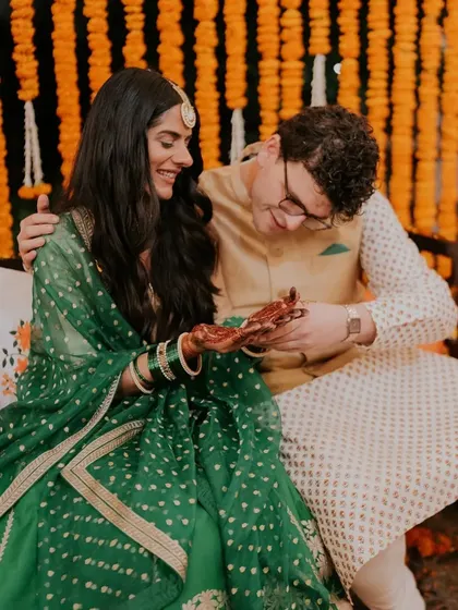 A happy couple during their mehndi ceremony, with the groom admiring the bride's freshly stained henna.
