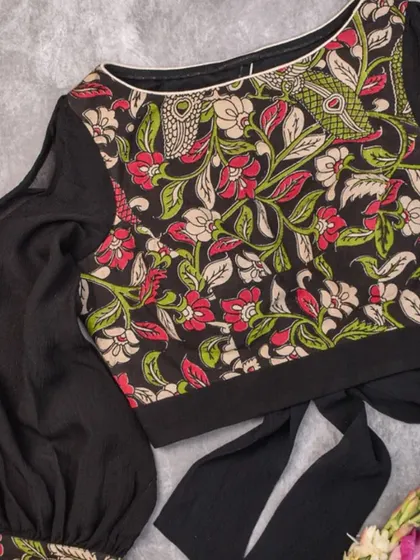 A unique blouse featuring a black body with sheer, billowy sleeves and a Kalamkari-printed front panel. The tie-back detail adds a modern touch.