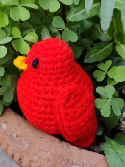 A little red bird plushie, perfect for sitting on a shelf or in a plant pot.
