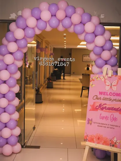 A welcoming entrance for a butterfly-themed birthday party, with a pink and purple balloon arch and a custom sign.