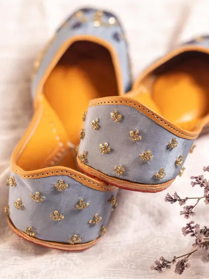 A pair of light blue juttis styled with delicate flowers. This soft, romantic aesthetic is perfect for bridal or special occasion wear, and we tailor our styling to match the product's intended market.