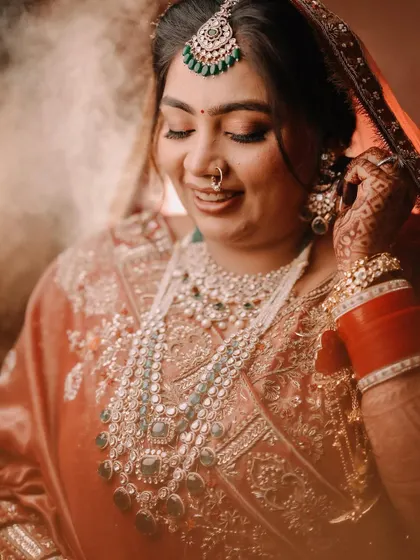 A close-up shot of the bride adjusting her earring. This candid-style portrait captures a quiet, personal moment of getting ready, focusing on the intricate details of her jewelry and her serene expression.