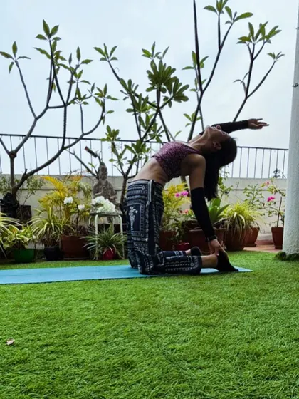 Camel pose with one arm reaching back, the terrace plants framing the shot.