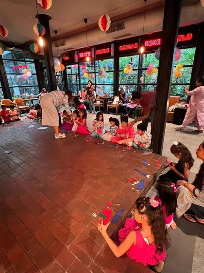 A wide shot of a party in a beautiful, open venue. Our team is seen guiding a large group of children as they sit on the floor, engrossed in their building activity.