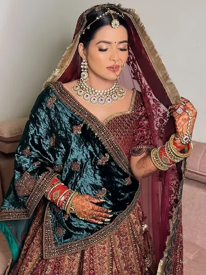 An ethereal beauty in her bridal attire. This look features a deep maroon velvet lehenga, and the makeup is kept classic with soft smokey eyes and a matching lip color.