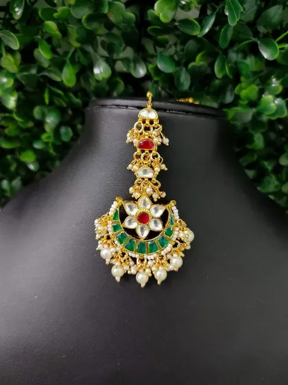 A lovely crescent-shaped maang tikka with a central floral motif. The combination of red and green stones makes it a classic choice for brides.