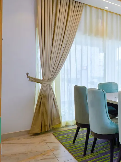 A calm and elegant dining area with subtle green chairs, a marble-top table, and a wooden crockery unit.