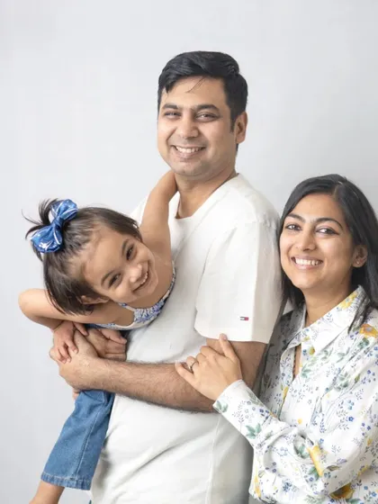 A playful family portrait against a simple white background. The daughter's happy, upside-down pose adds a touch of fun and personality.