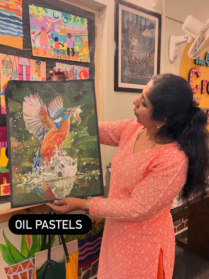 I'm holding up a dynamic oil pastel drawing of a kingfisher. While we focus on acrylics, we also explore other mediums like pastels to broaden artistic skills.
