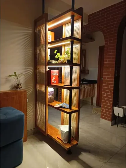 Partitions don't have to divide; they can add splendor. This custom-made wooden partition with integrated shelving and lighting acts as a stylish divider while also serving as a beautiful display unit for plants and books.