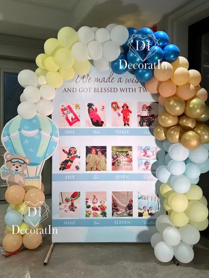 A milestone photo board celebrating the first year, framed by a colorful balloon arch.