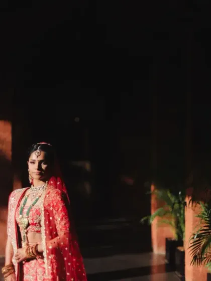 The bride stands in a corridor, the dramatic play of light and shadow highlighting her stunning red lehenga. This is an artistic and powerful bridal portrait.