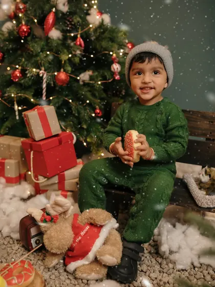 A happy little boy enjoys a Christmas cookie next to the tree.