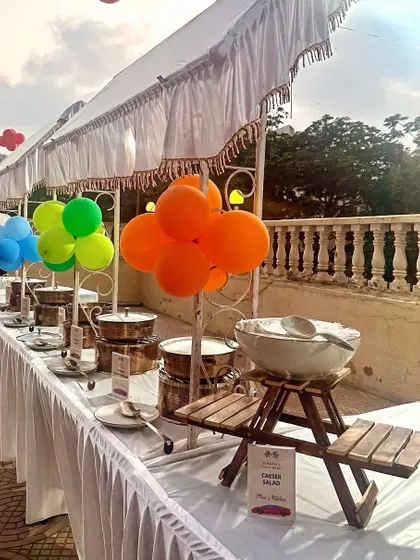 A colorful outdoor buffet setup for a kid's birthday party. The bright balloons tied to the serving stations add a playful touch that matches the fun atmosphere of the event.