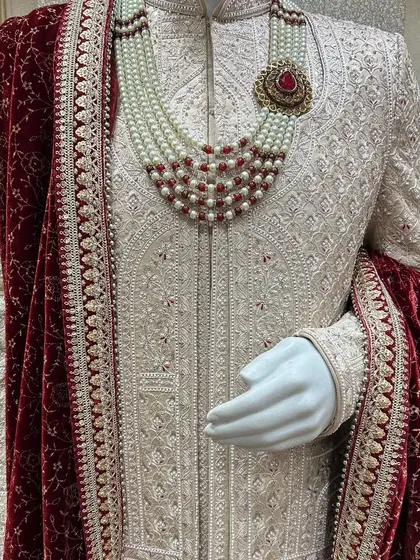 A closer look at the royal treatment. This ivory sherwani features detailed embroidery, paired with a rich red velvet stole and a multi-layered pearl necklace. I focus on these details to give you a truly regal look for your wedding day.