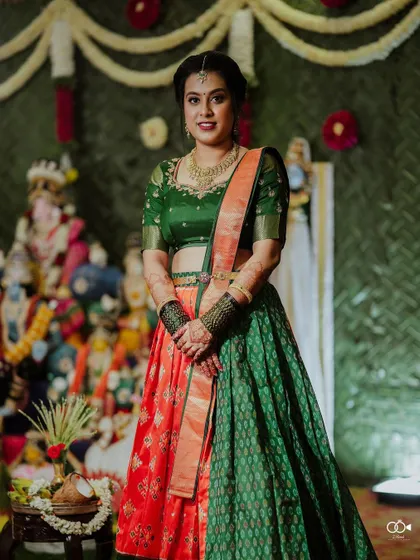 A full-length portrait of the bride in her colorful half-saree, posing in front of the traditional Golu display.