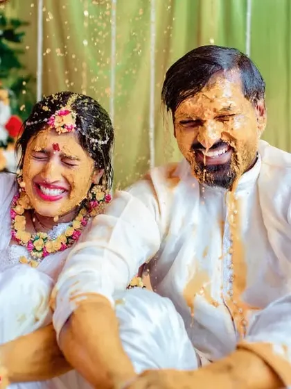 A candid shot of a couple covered in turmeric, laughing together. We focus on capturing the real, messy, and beautiful moments of the Haldi ceremony.