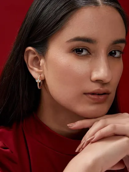 A close-up beauty shot highlighting a pair of sparkling hoop earrings. The pose is classic and graceful, perfect for showcasing fine jewelry.