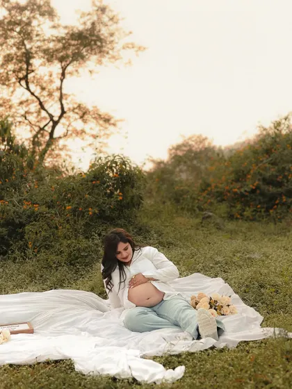 A serene solo portrait of the mother-to-be at the picnic. She lies back on the blanket, gently cradling her bare bump, connecting with her baby amidst nature.