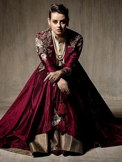 A full-length portrait showcasing a layered Indo-western outfit. The seated pose allows the rich, velvet-like fabric to pool around the model, emphasizing its texture and luxurious feel.