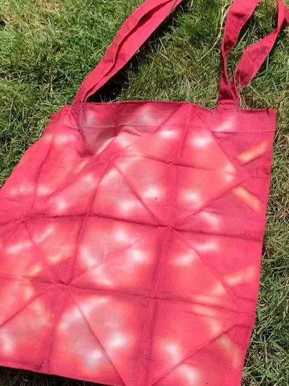 Another view of the red tie-dyed tote bag, lying on the grass. It's a functional piece of art that you can use every day.