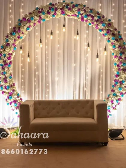 A simple yet stunning engagement photo booth. This setup features a full floral circle in white, purple, and blue, with hanging Edison bulbs that create a warm, inviting glow for beautiful pictures.
