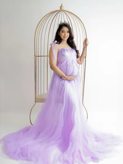A fairytale portrait with a golden birdcage prop. The mom-to-be looks like a princess in her flowing lavender gown and tiara.