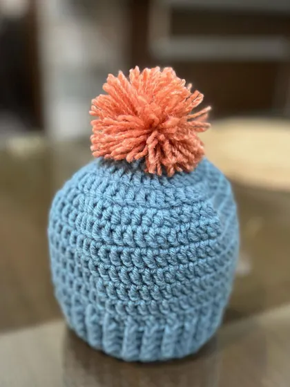 A single shot of this adorable blue baby beanie with a contrasting pom-pom. It's made from soft, breathable cotton yarn, making it comfortable for a baby to wear.