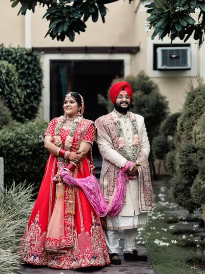 A traditional wedding portrait of the Sikh couple. They stand together, holding the ceremonial palla, symbolizing their union in a classic and beautifully composed photograph.