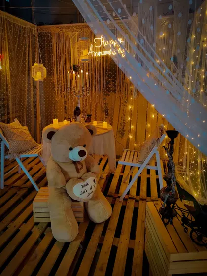 This is a wider view of my popular Macrame Bliss setup, perfect for an anniversary surprise. The combination of wooden pallets, soft lighting, and a giant teddy bear creates a scene that is both rustic and heartwarming.