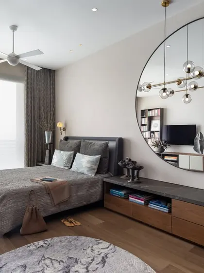 A full view of the guest bedroom, showcasing its thoughtful layout. The large circular mirror is a key design element, reflecting light and the room's sculptural details, making the space feel larger and more dynamic.