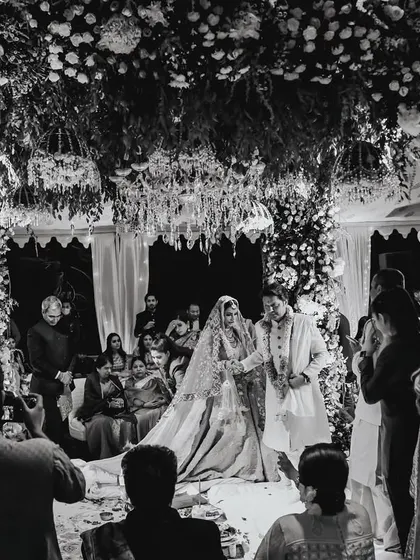A wide, atmospheric shot of the Pheras ceremony in black and white, capturing the solemnity and beauty of the moment under a floral mandap.