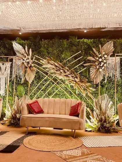 A full view of our nature-inspired boho stage for Anuja and Amit. The combination of a green wall, macrame, dried grasses, and natural fiber rugs creates a warm, earthy, and incredibly stylish setting.