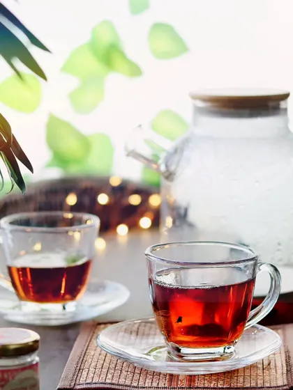 Two clear glass cups of black tea, with a teapot in the background against bright, airy lighting. This shot feels modern, clean, and refreshing.