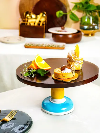 A vibrant wooden and ceramic cake stand styled with pastries on a fully set table. This shot shows the product in its intended environment, surrounded by other complementary tableware.