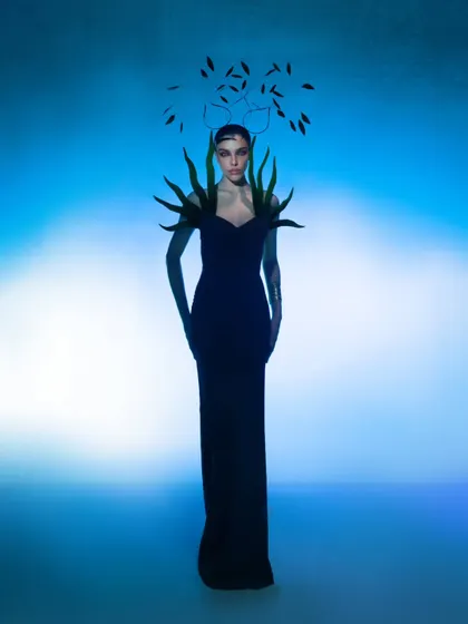 A full-length shot showcasing a dramatic silhouette against a vibrant blue backdrop. The styling and pose create a powerful, otherworldly character.