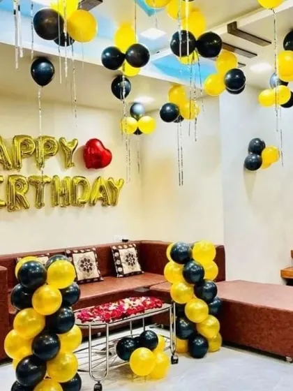 A full room decoration for a birthday in black and yellow, with balloons on the ceiling and balloon pillars.