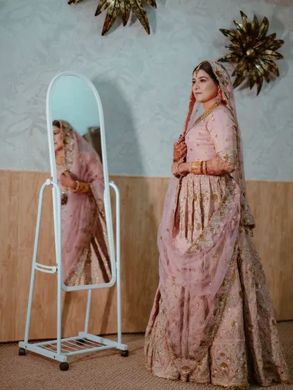 A full-length portrait of the bride in her elegant pink Nikkah outfit, her reflection adding a layer of depth to the image.