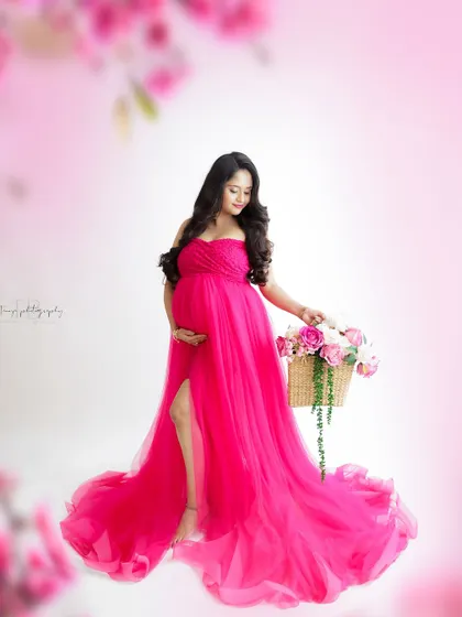 A vibrant and joyful portrait. The mom-to-be is surrounded by a soft pink glow, her bright pink gown and basket of flowers creating a stunning image.