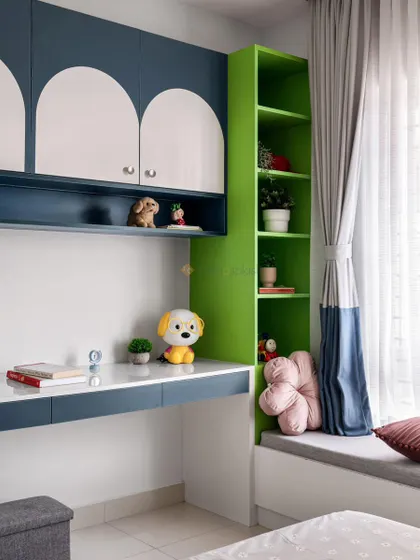 This kid's room features a custom study desk with blue and white arched cabinets and a vibrant green bookshelf. The cozy window seat is perfect for reading.