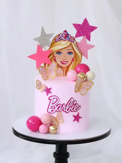 A glamorous Barbie cake for a little princess. This pink cake is decorated with stars, butterflies, and shimmering spheres, featuring a stylish Barbie topper.