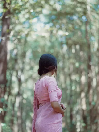 An artistic shot from behind, focusing on the model in a pink saree against a blurred forest background. It creates a sense of mystery and serenity.
