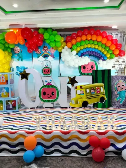 A cheerful and colorful Cocomelon party stage, featuring a rainbow balloon arch, the iconic yellow school bus, and cutouts of all the favorite characters.
