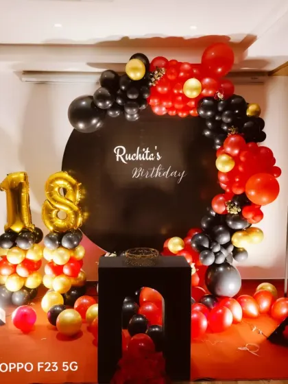 A bold and glamorous 18th birthday celebration. The decor uses a striking red, black, and gold color scheme with a balloon arch over a personalized black backdrop.