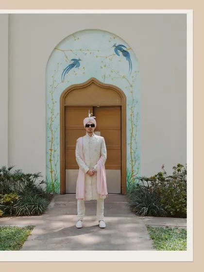 A full-length portrait of the groom looking sharp and stylish in his wedding attire, standing before a beautifully painted archway.
