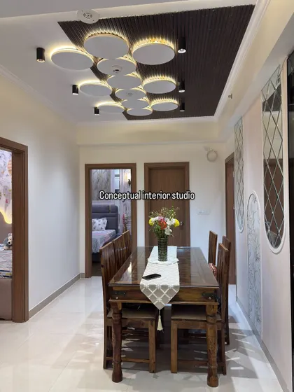 A view of the dining area, showcasing the modern false ceiling with unique circular light fixtures and track lights that provide ample, stylish illumination.