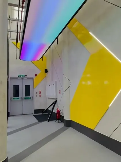 An iridescent, color-changing light panel adds a futuristic and dynamic element to the gym's corridor. This feature contrasts with the static yellow wall panels, creating a memorable visual moment.